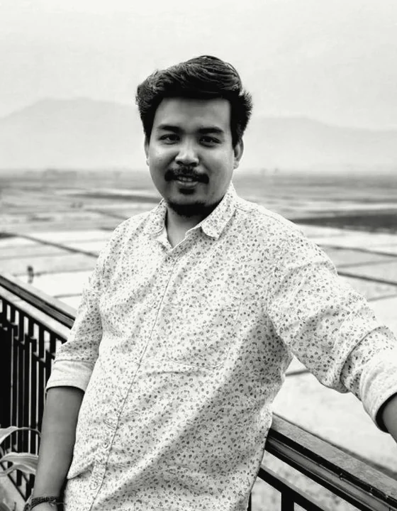 Dhiraj Hazarika, in a patterned shirt, leaning on a railing above rice fields.